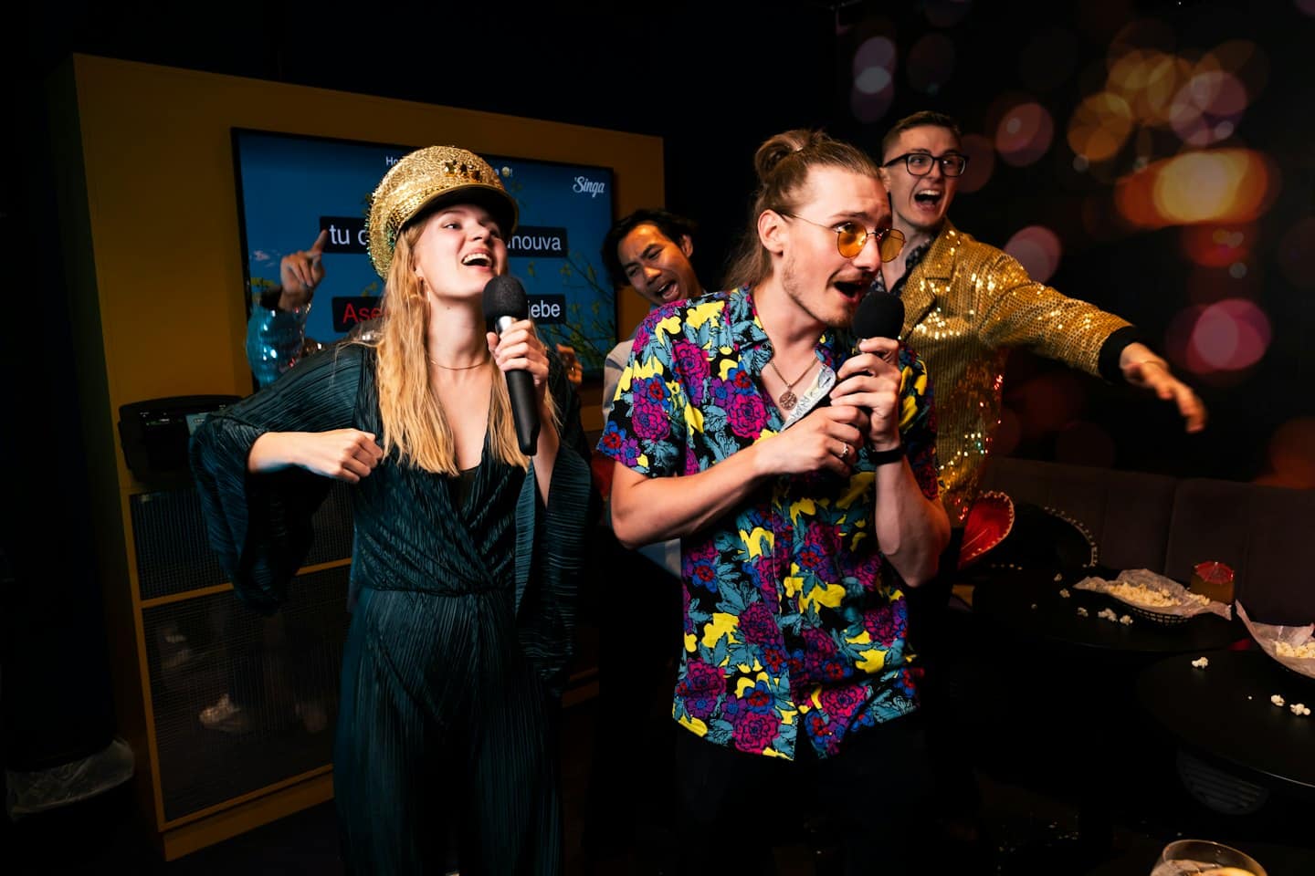 Quattro amici cantano allegramente al karaoke con microfoni in una stanza moderna.