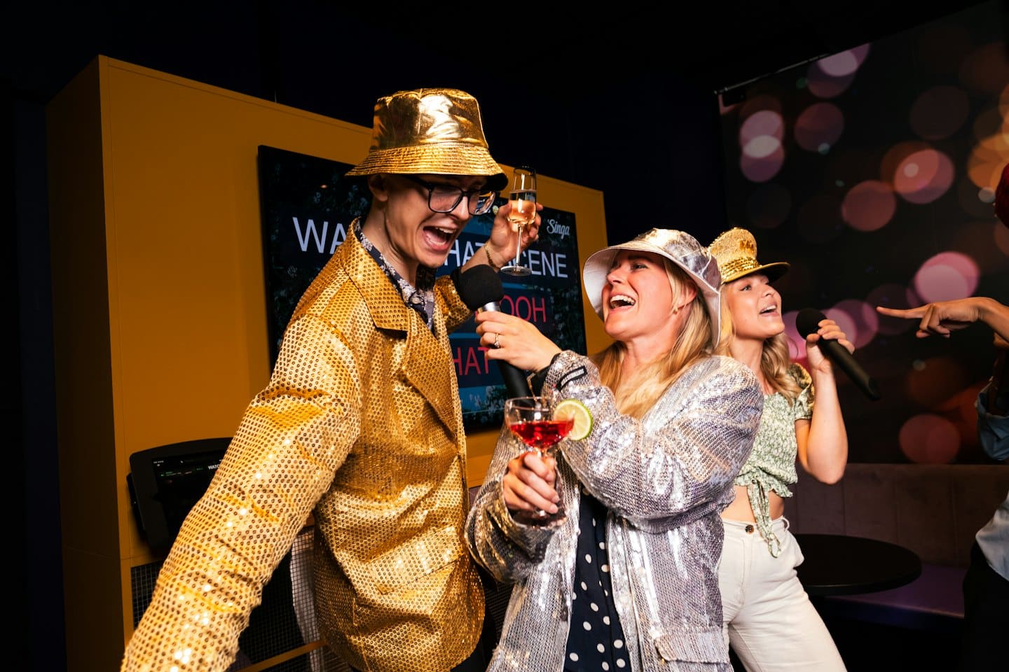 Amici che cantano al karaoke vestiti in modo festivo e con in mano da bere.