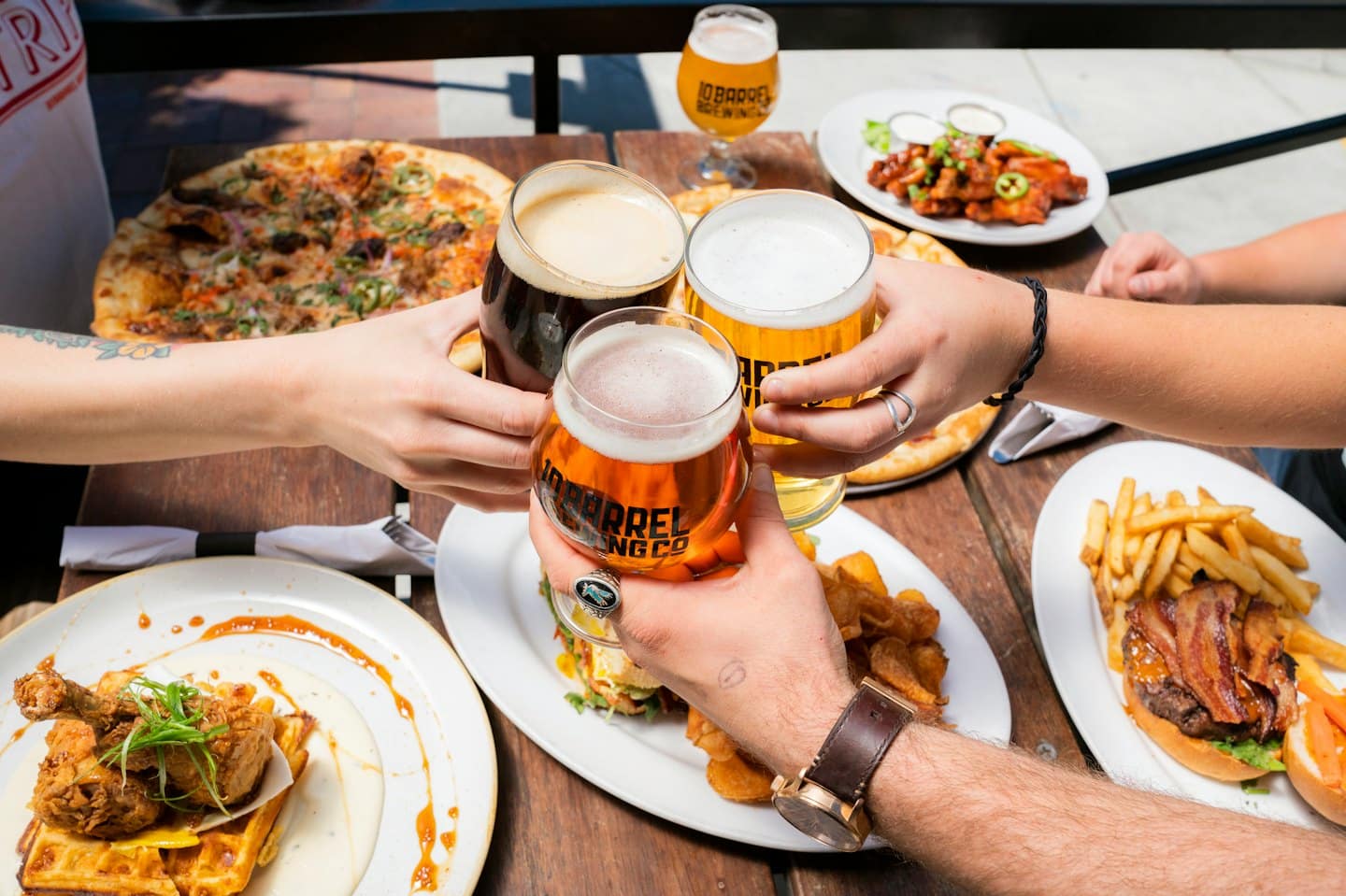 Amici che tintinnano bicchieri di birra su un tavolo pieno di cibo.