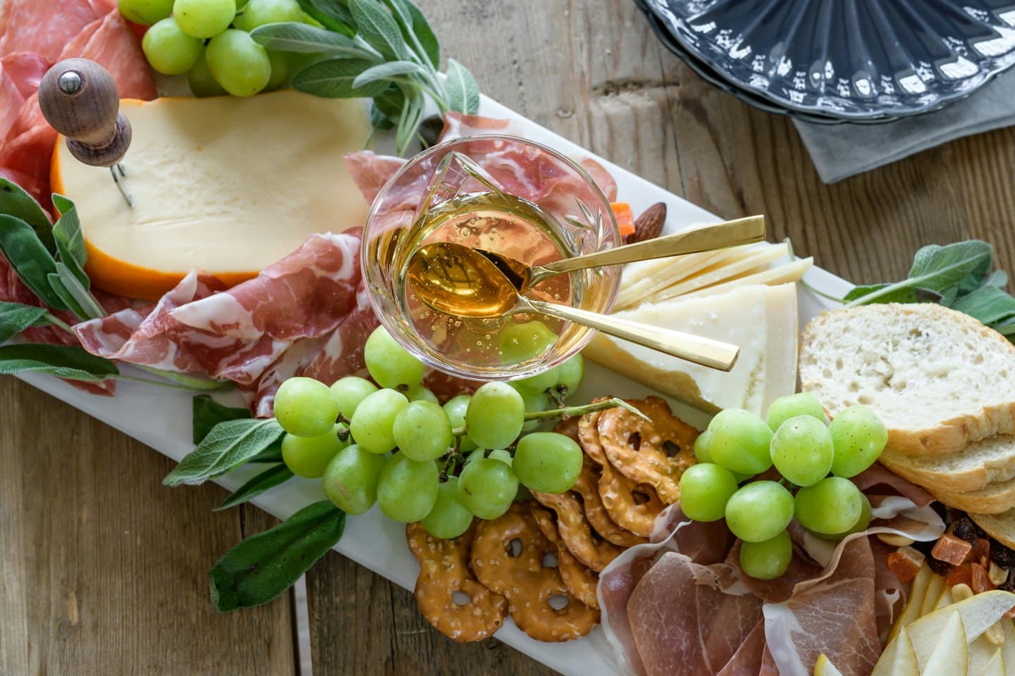 Tagliere di salumi con uva, salumi, formaggio e pretzel.