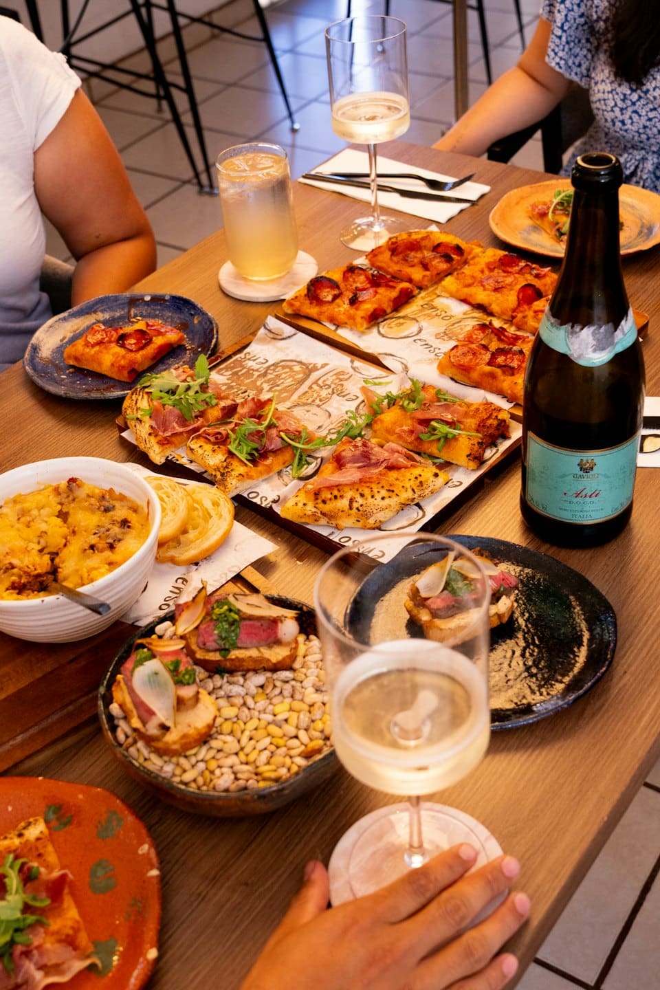 Persone che condividono pizza, pasta e vino italiani a tavola.