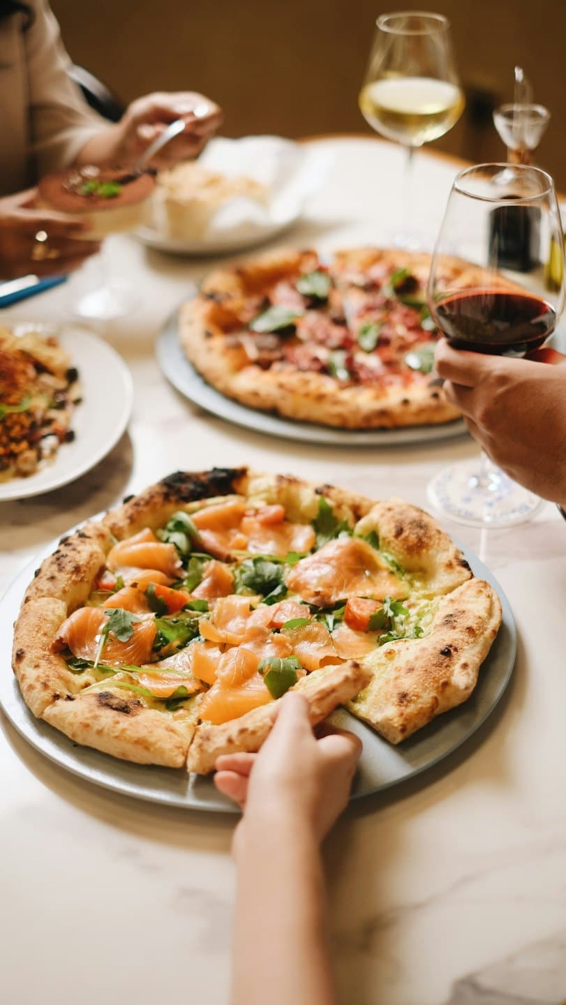 Amici che condividono pizze gourmet e vino a un tavolo da pranzo.